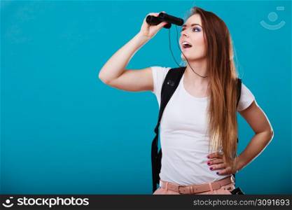 Summer holidays and tourism concept. Attractive woman long hair with backpack looking through binocular on blue