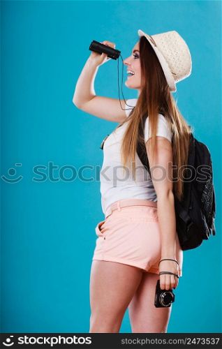 Summer holidays and tourism concept. Lovely tourist woman with backpack looking through binoculars on blue sideview