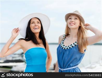 summer holidays and vacation concept - girls in dresses with hats on the beach