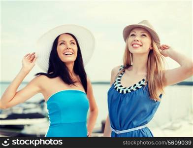 summer holidays and vacation concept - girls in dresses with hats on the beach