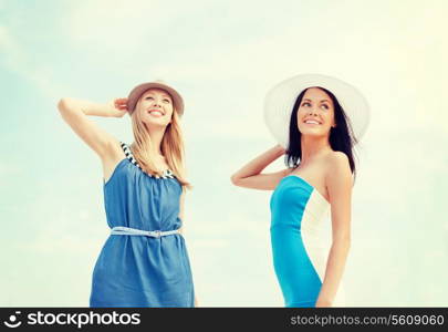 summer holidays and vacation concept - girls in dresses with hats on the beach