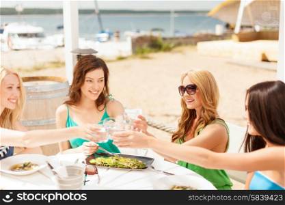 summer holidays and vacation concept - girls making a toast in cafe on the beach. smiling girls looking at tablet pc in cafe