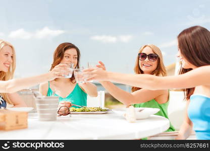 summer holidays and vacation concept - girls making a toast in cafe on the beach. smiling girls looking at tablet pc in cafe