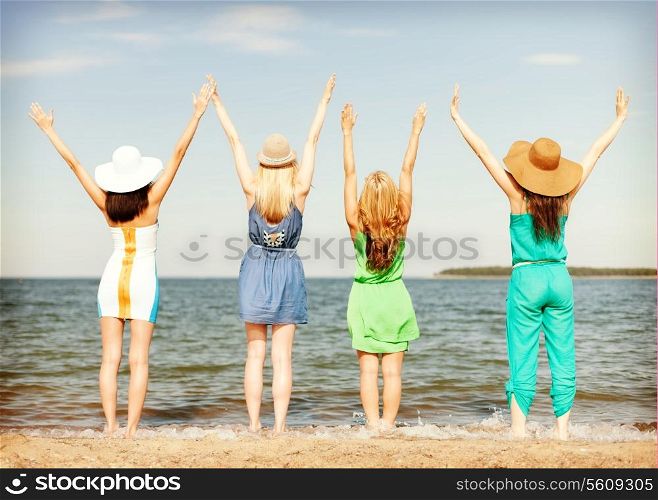 summer holidays and vacation concept - girls with hands up on the beach