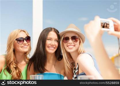 summer holidays and vacation concept - smiling girls taking photo with digital camera in cafe on the beach