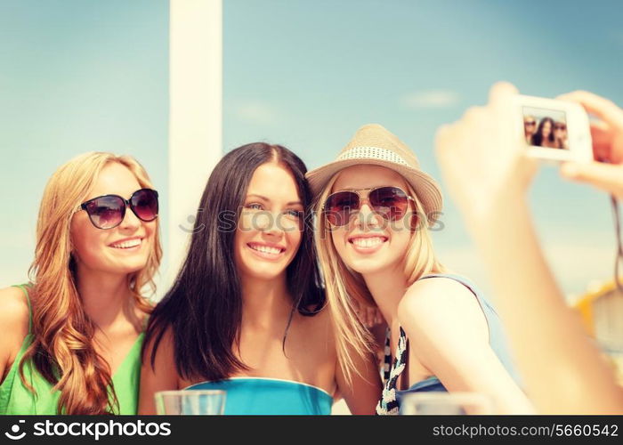 summer holidays and vacation concept - smiling girls taking photo with digital camera in cafe on the beach