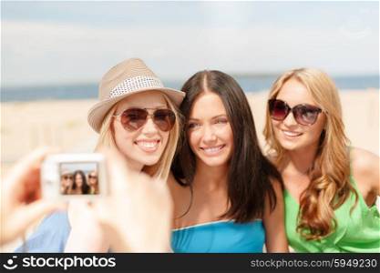 summer holidays and vacation concept - smiling girls taking photo with digital camera in cafe on the beach. girls taking photo with digital camera in cafe