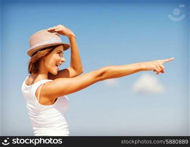 summer holidays and vacation - girl in hat showing direction on the beach
