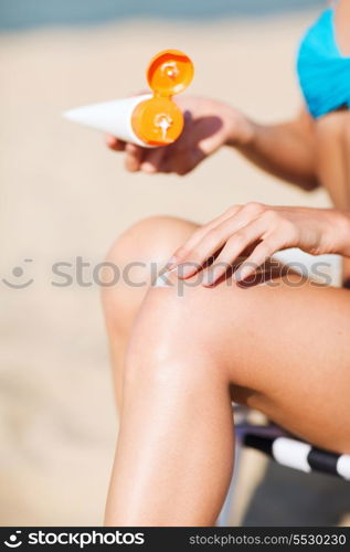 summer holidays and vacation - girl putting sun protection cream on the beach chair