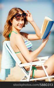 summer holidays and vacation - girl reading book on the beach chair