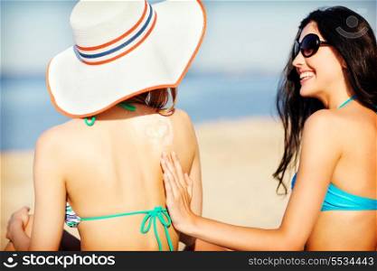 summer holidays and vacation - girls applying sun protection cream on the beach