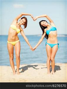 summer holidays and vacation - girls in bikinis making heart shape with hands on the beach