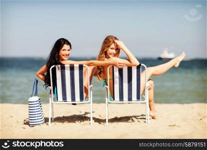 summer holidays and vacation - girls in bikinis sunbathing on the beach chairs. girls sunbathing on the beach chairs