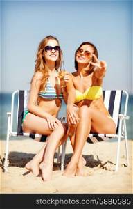 summer holidays and vacation - girls in bikinis with drinks on the beach chairs