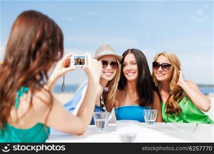 summer holidays and vacation - girls taking photo with digital camera in cafe on the beach. girls taking photo in cafe on the beach