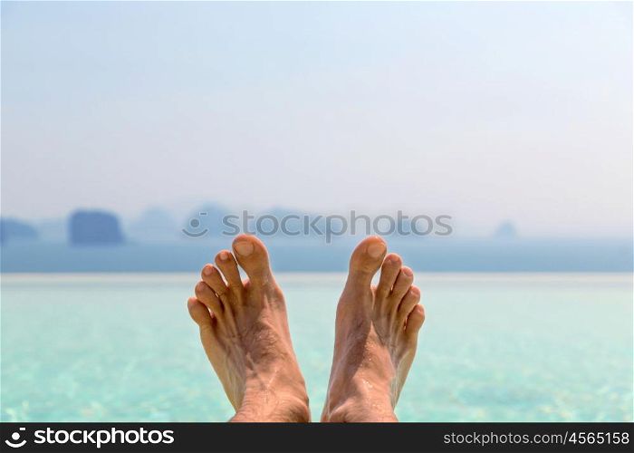 summer holidays, beach, travel, leisure and body care concept - closeup of male feet over sea and sky