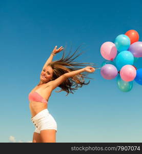 Summer holidays, celebration and happiness concept - attractive athletic woman teen girl jumping with colorful balloons hair blowing on wind outdoors sunny day, blue sky background