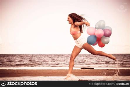 Summer holidays, celebration and lifestyle concept - attractive athletic woman teen girl jumping with colorful balloons outside on beach, aged retro tone