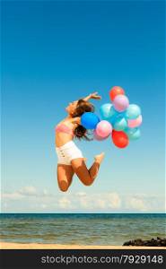 Summer holidays, celebration and lifestyle concept - attractive athletic woman teen girl jumping with colorful balloons outside on beach, sunny day
