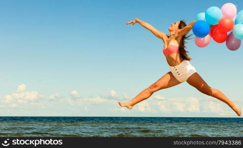 Summer holidays, celebration and lifestyle concept - attractive athletic woman teen girl jumping with colorful balloons outside on beach, sunny day