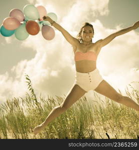 Summer holidays, celebration and lifestyle concept - beautiful athletic woman teen girl jumping with colorful balloons outside on beach. aged vintage tone