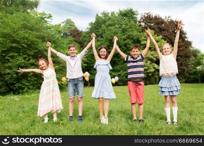 summer holidays, childhood and frinedship concept - happy kids holding hands in park. happy kids holding hands in summer park. happy kids holding hands in summer park