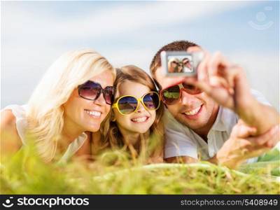 summer holidays, children and people concept - happy family with camera, blue sky and green grass taking picture