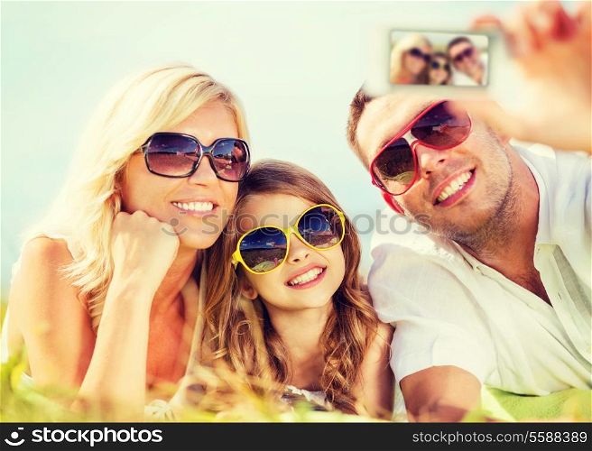 summer holidays, children and people concept - happy family with camera, blue sky and green grass taking picture
