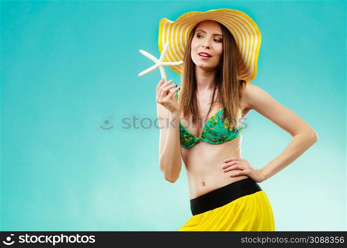 Summer holidays concept. Closeup woman in yellow hat bikini holding white shell starfish in hand on vivid blue background