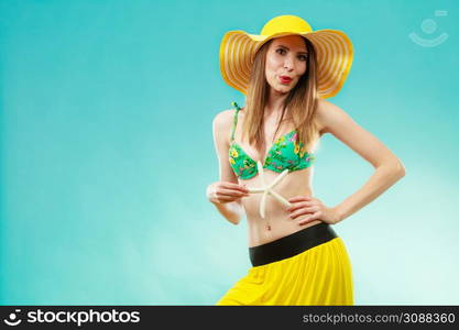 Summer holidays concept. Closeup woman in yellow hat bikini holding white shell starfish in hand on vivid blue background