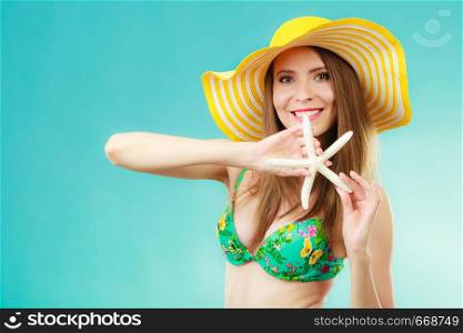 Summer holidays concept. Closeup woman in yellow hat bikini holding white shell starfish in hand on vivid blue background