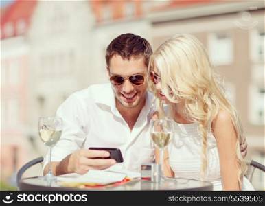 summer holidays, dating and technology concept - couple looking at smartphone in cafe in the city