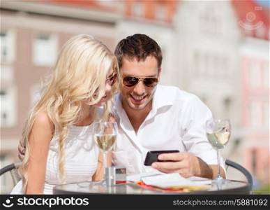 summer holidays, dating and technology concept - couple looking at smartphone in cafe in the city