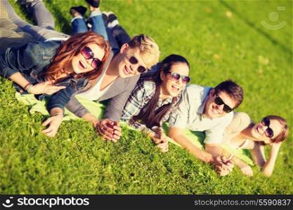 summer holidays, education and teenage lifestyle concept - group of students or teenagers lying on grass in park