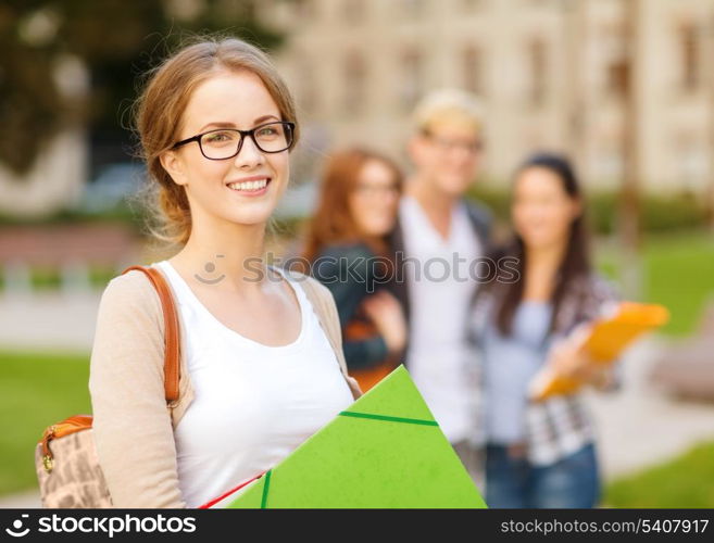 summer holidays, education, campus and teenage concept - smiling female student in black eyeglasses with folders and group in the back