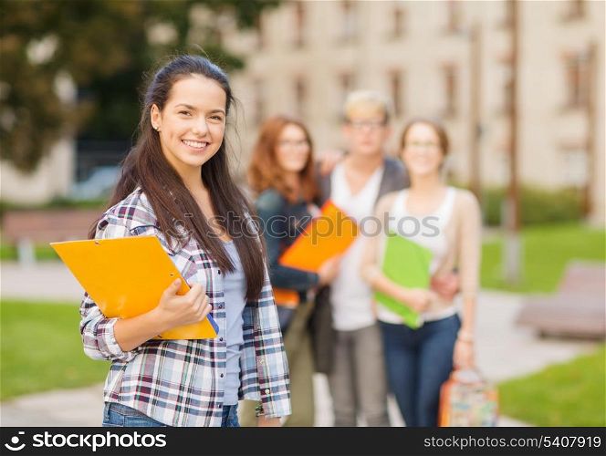 summer holidays, education, campus and teenage concept - smiling female student in with folders and group in the back