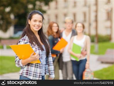 summer holidays, education, campus and teenage concept - smiling female student in with folders and group in the back
