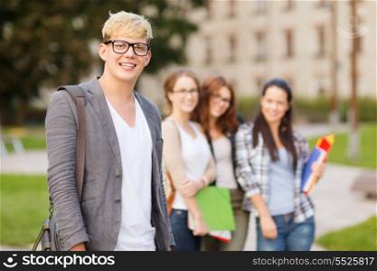 summer holidays, education, campus and teenage concept - smiling teenage boy in eyeglasses with classmates on the back
