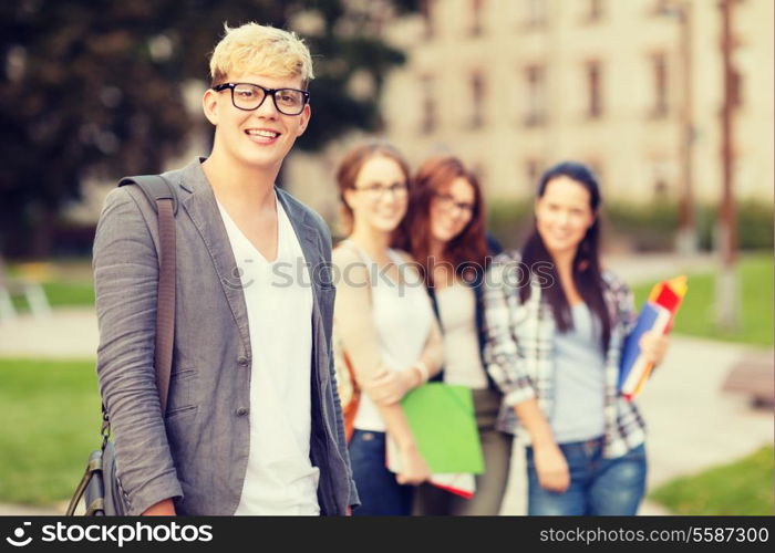 summer holidays, education, campus and teenage concept - smiling teenage boy in eyeglasses with classmates on the back