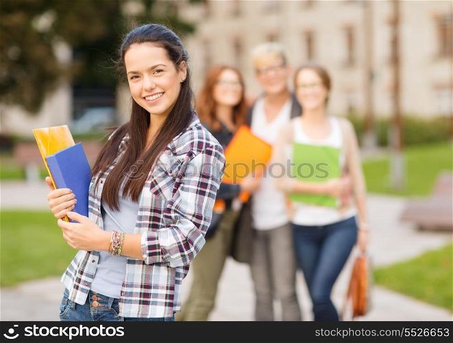 summer holidays, education, campus and teenage concept - smiling teenage girl with folders and classmates on the back