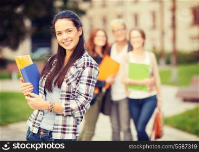 summer holidays, education, campus and teenage concept - smiling teenage girl with folders and classmates on the back