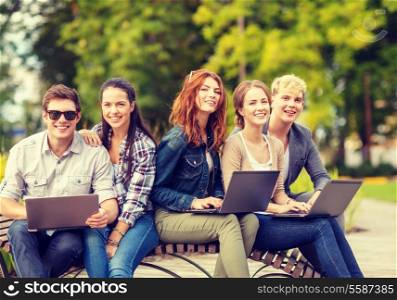 summer holidays, education, campus, technology and teenage concept - group of students or teenagers with laptop computer