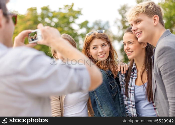 summer holidays, electronics and teenage concept - group of smiling teenagers taking photo with digital camera outside