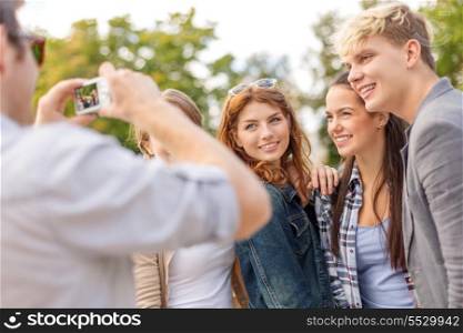summer holidays, electronics and teenage concept - group of smiling teenagers taking photo with digital camera outside