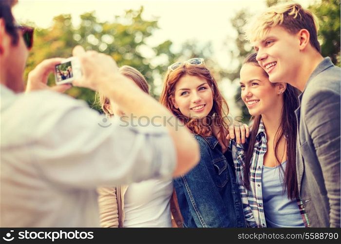 summer holidays, electronics and teenage concept - group of smiling teenagers taking photo with digital camera outside