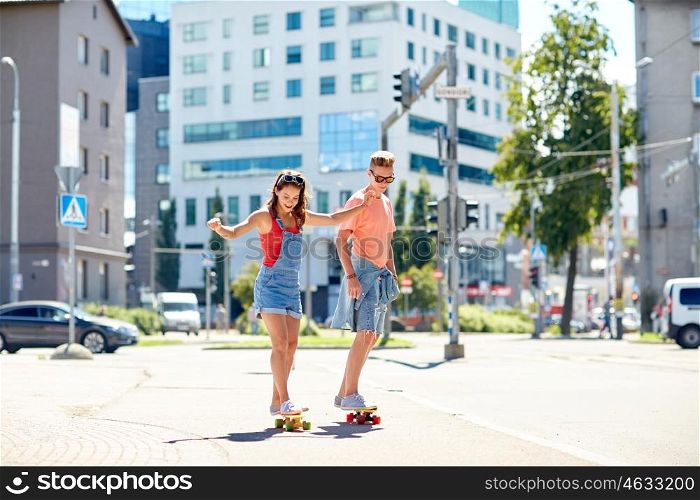summer holidays, extreme sport and people concept - happy teenage couple riding short modern cruiser skateboards on city street