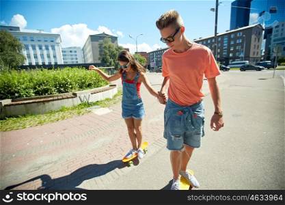 summer holidays, extreme sport and people concept - happy teenage couple riding short modern cruiser skateboards on city street