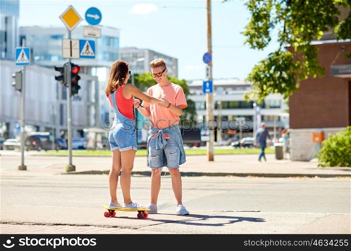 summer holidays, extreme sport and people concept - happy teenage couple riding short modern cruiser skateboard on city street