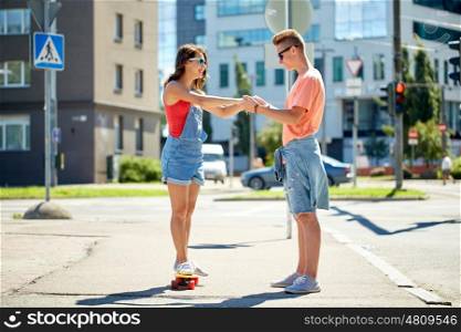 summer holidays, extreme sport and people concept - happy teenage couple riding short modern cruiser skateboard on city street