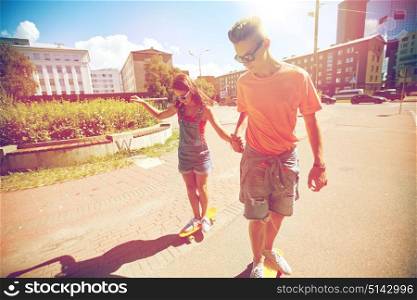 summer holidays, extreme sport and people concept - happy teenage couple riding short modern cruiser skateboards on city street. teenage couple riding skateboards on city street